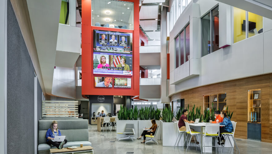 students in the atrium of building studying with tv's in background