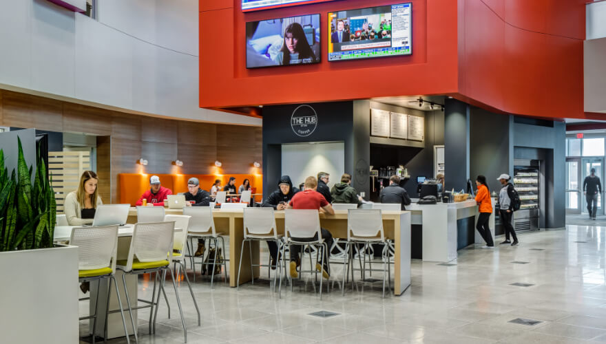 students in the atrium of building studying with tv's in background