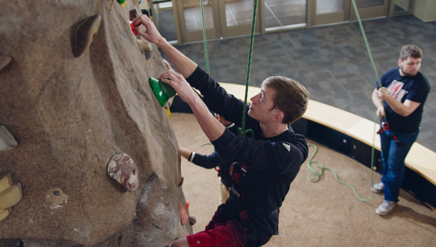 student rock climbing on rock wall on belay
