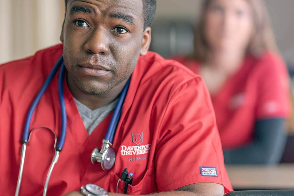 A male student in red Davenport University scrubs with a stethoscope around his neck.