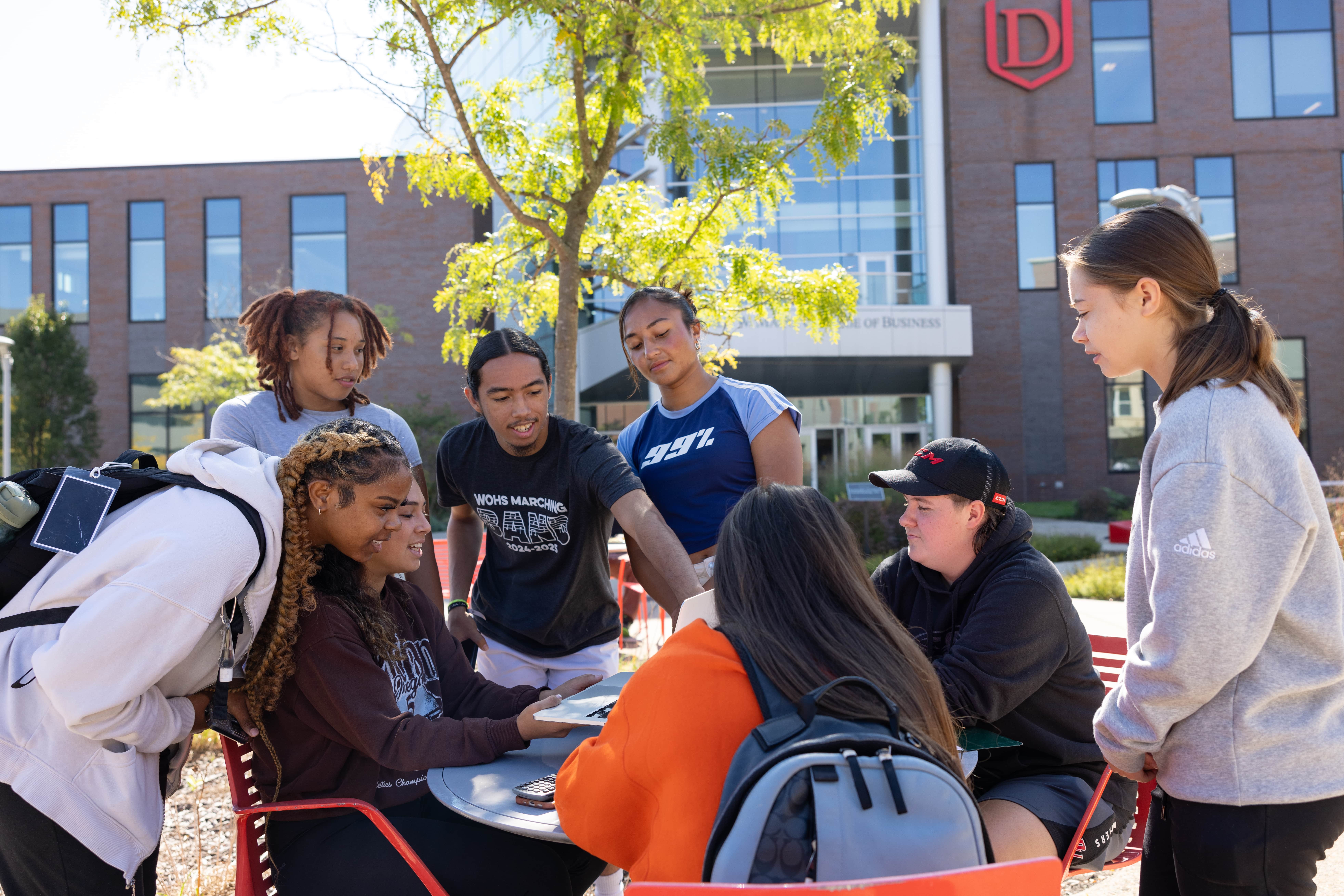 A group of students gathered around a table outside on the College of Business