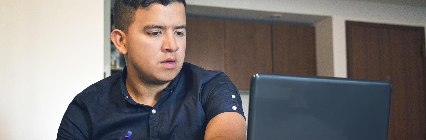 Male on his laptop and writing in a notebook