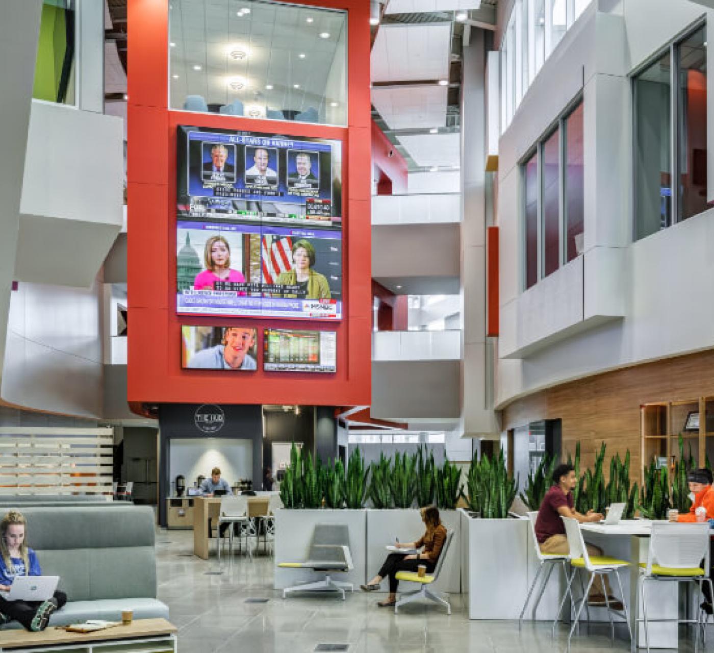 students in the atrium of building studying with tv's in background