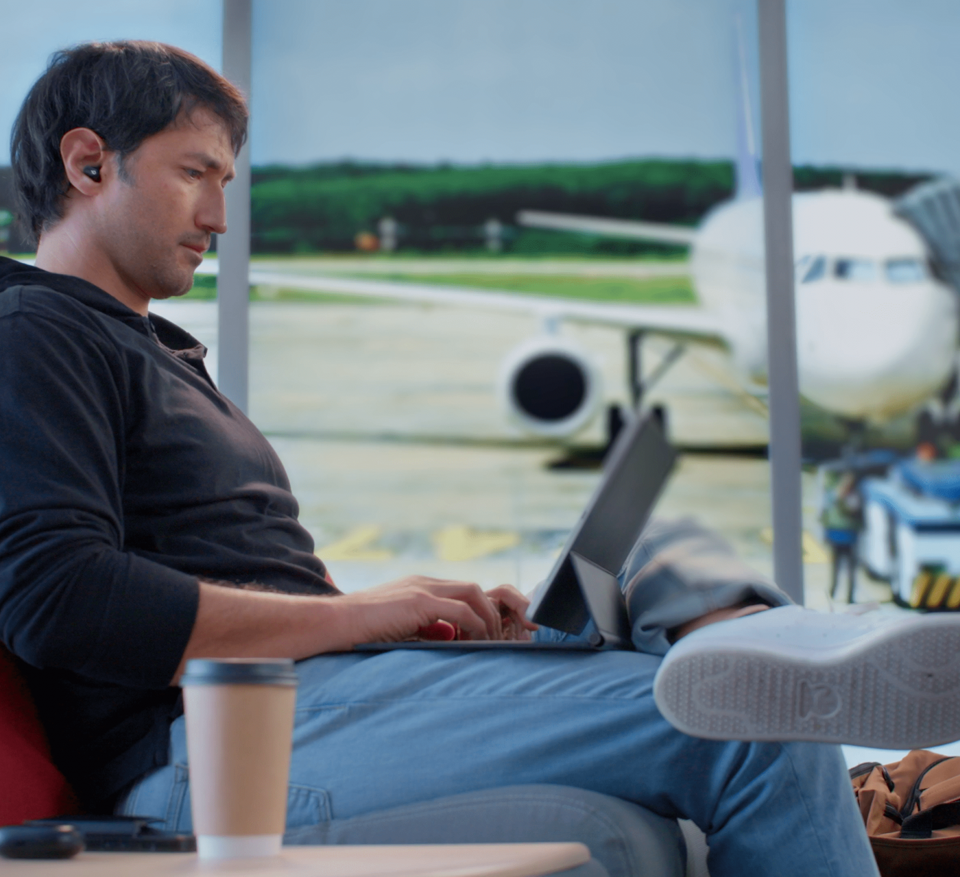 Male in an airport lounge on his computer with a plane in the background