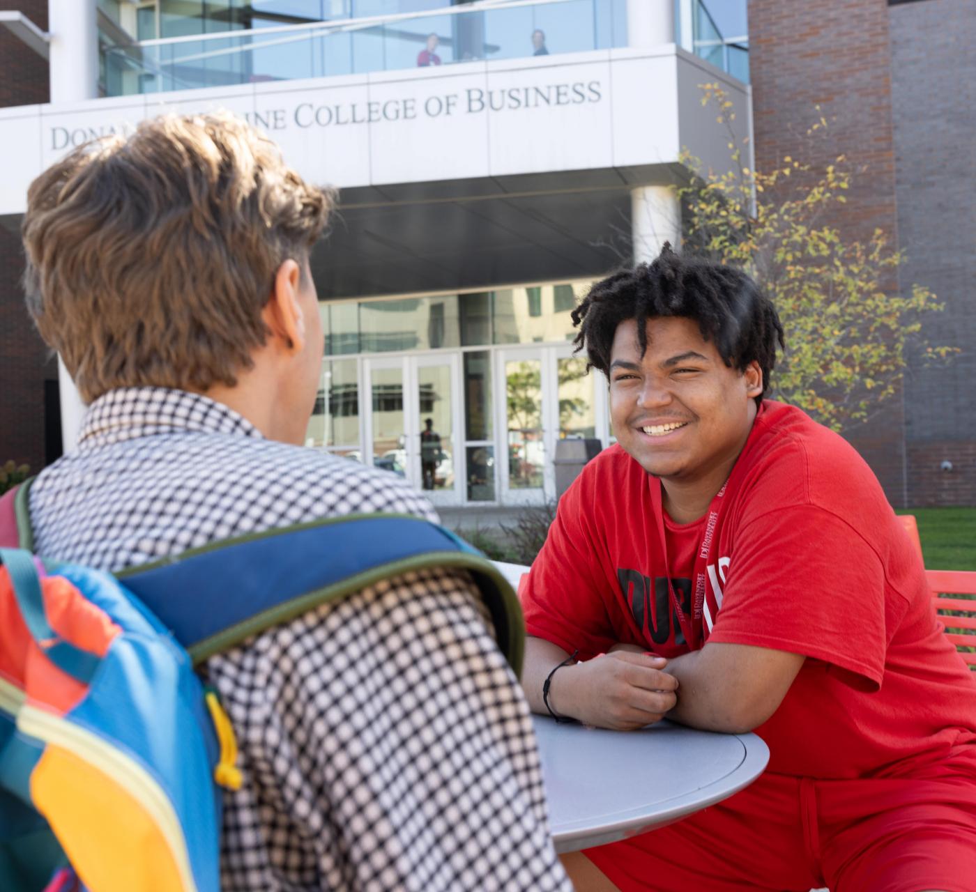 Two male students at a table on the W.A. Lettinga campus outside the College of Business building