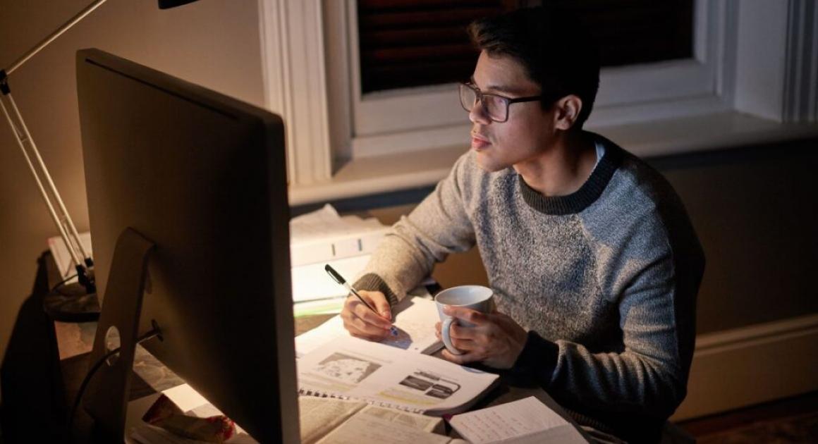 man looking at computer while writing on notebook