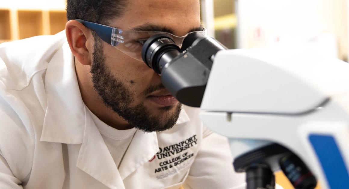 Student in a lab coat looking through a microscope