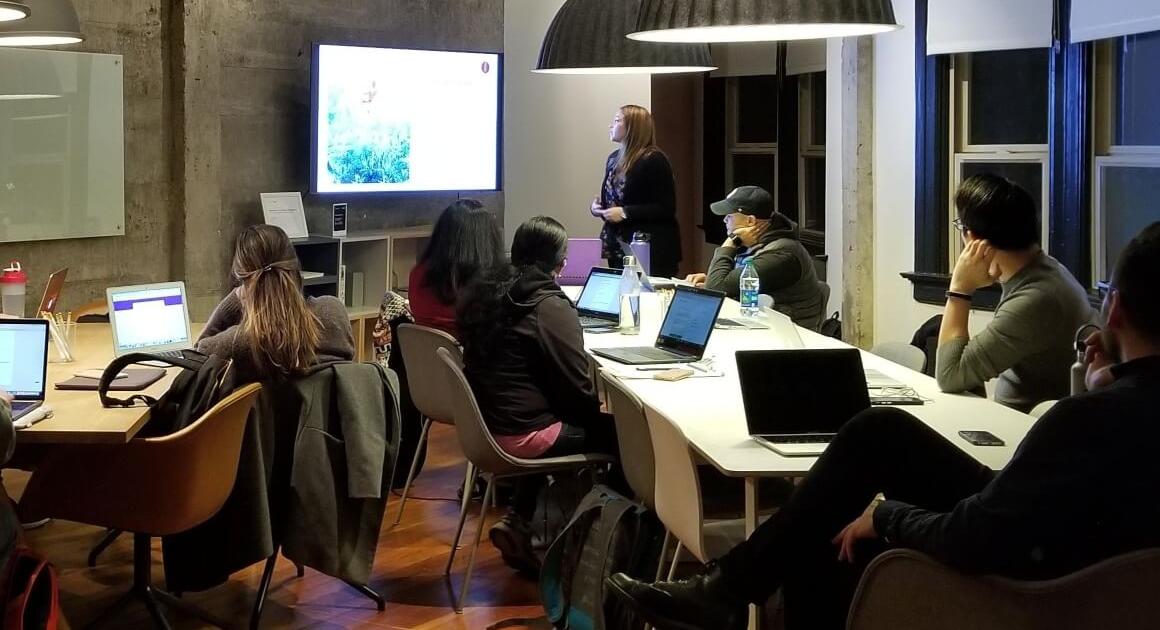 Students at long tables looking at a TV screen