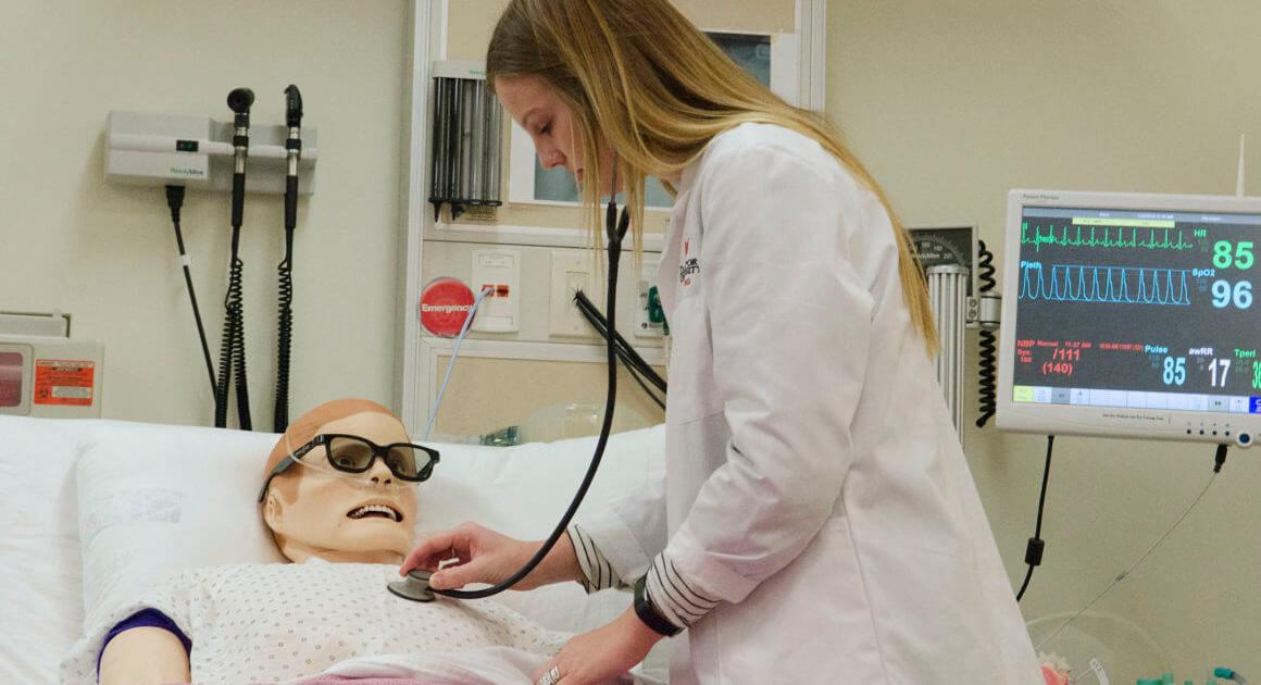 Student with a white coat and stethoscope in a hospital room