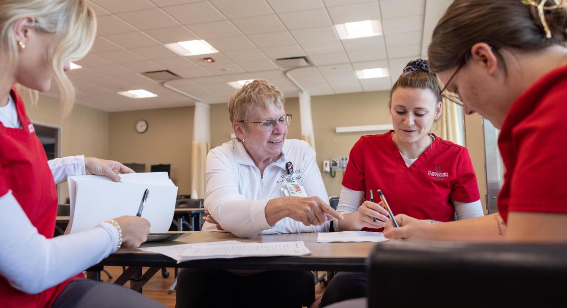 Three nursing students studying and meeting with a nursing professor 