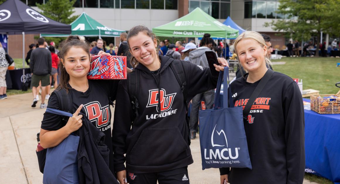 Three female students with Davenport Lacrosse sweatshirts at a campus event