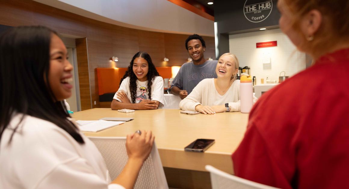 A group of students around a table at the HUB laughing 