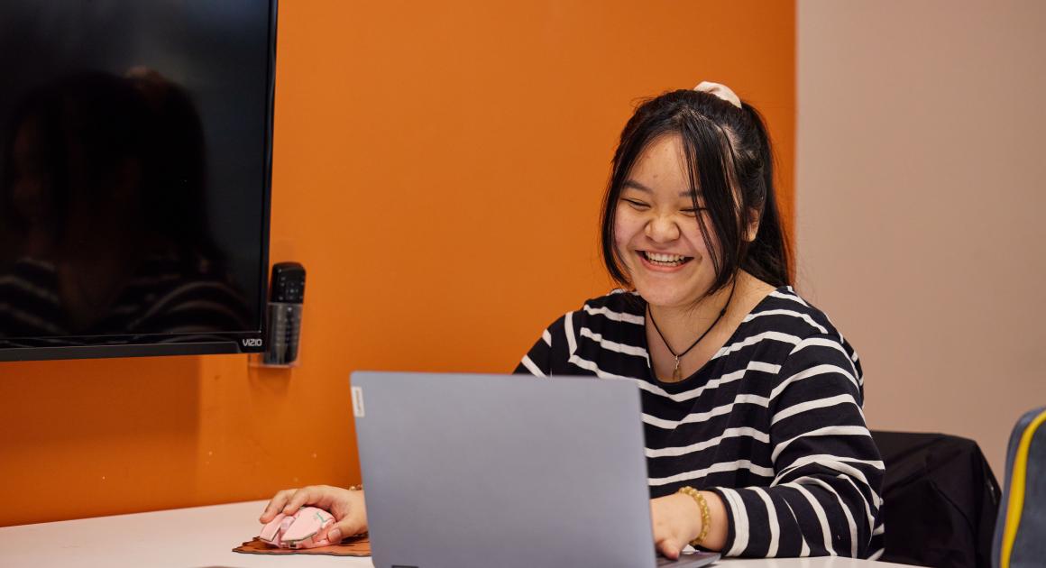 A young female student on their computer smiling 