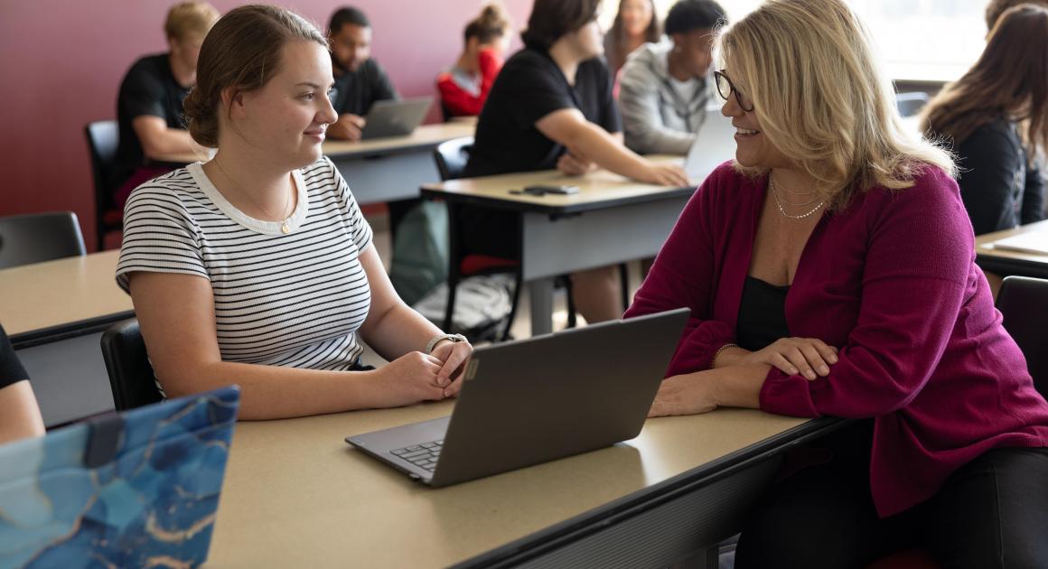 A photo of a classroom focused on a female student and female professor having a conversation