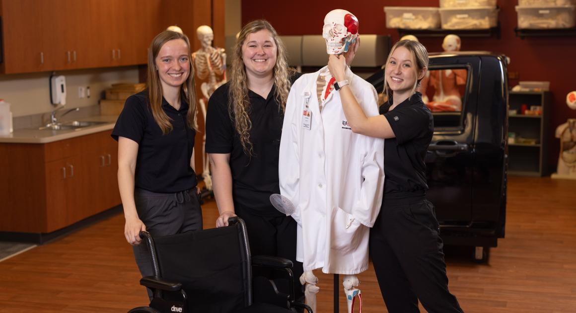 Three female OT students with a fun skeleton dressed in a medical coat
