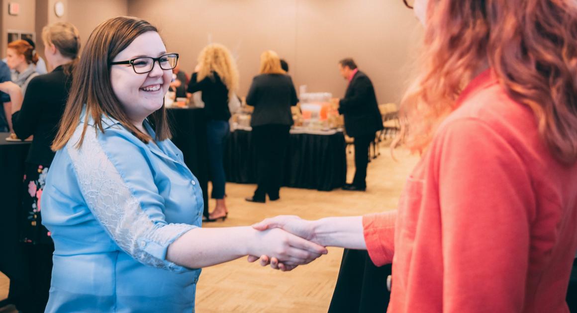 Female student in professional attire shaking a women's hand at an event