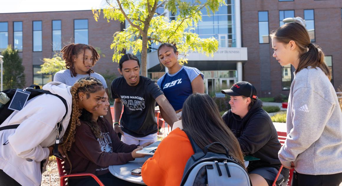 A group of students gathered around a table outside on the College of Business